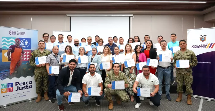 Grupo de personas sonrientes sosteniendo un diploma junto con los banners de OIT "Pesca Justa" y el Ministerio de Trabajo del Ecuador