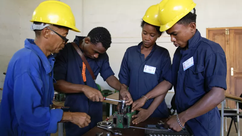 3 people wearing yellow helmets are learning new skills in mechanics