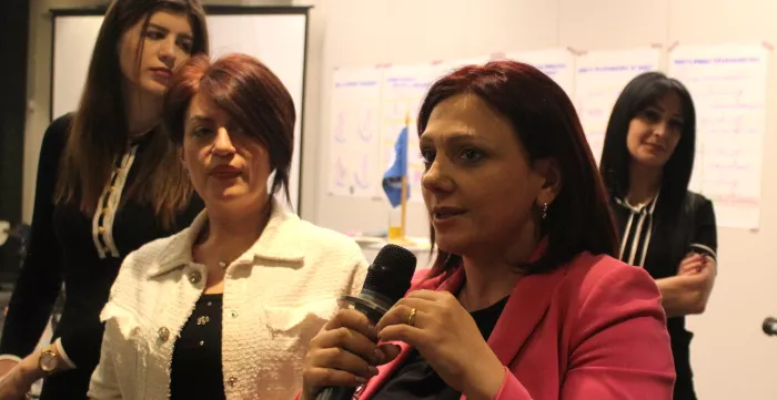 Four women stand in front of the board, one of them holds a microphone