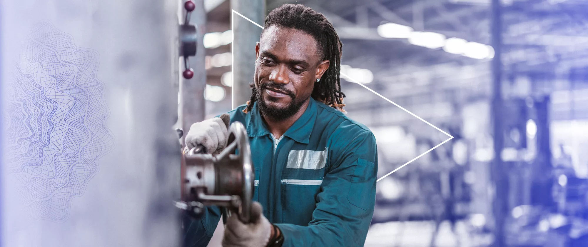 Man wearing a work uniform holds a machine wheel in a factory.